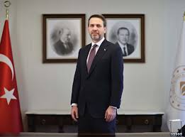 a man in a suit standing in front of two flags
