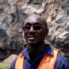 man in an orange vest standing in front of a mountain in Africa