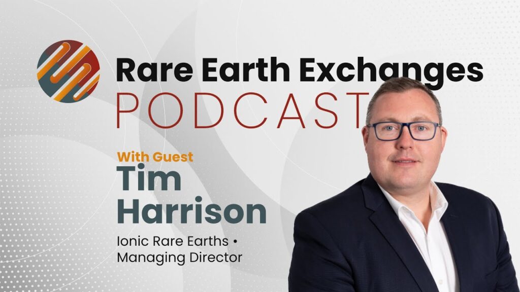 man in a suit and glasses standing in front of a sign