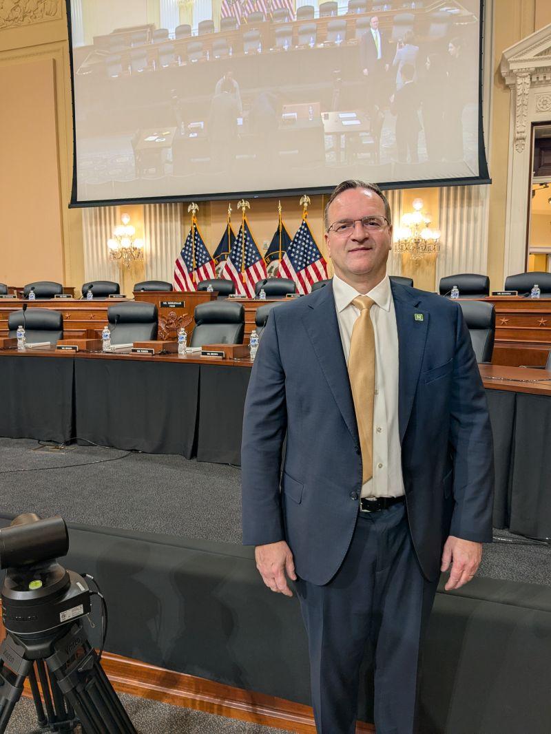 man in a suit standing in front of a large screen related to the domestic magnet supply chain
