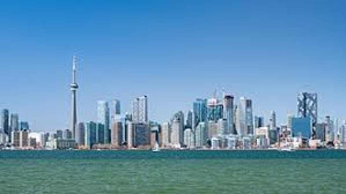 Toronto downtown skyline featuring the CN Tower rising above glass skyscrapers along the Lake Ontario waterfront on a clear d
