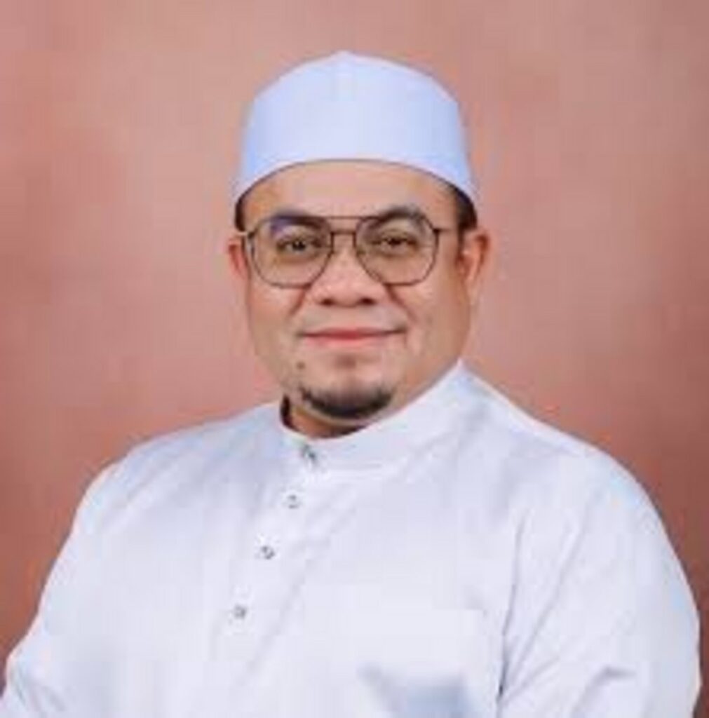 Middle-aged Muslim man wearing a white kufi cap, gold-framed glasses, and a white baju melayu, smiling softly against a warm
