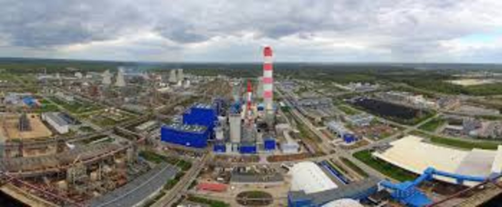 Panoramic aerial view of a vast industrial power plant complex with a tall red and white striped chimney stack surrounded by