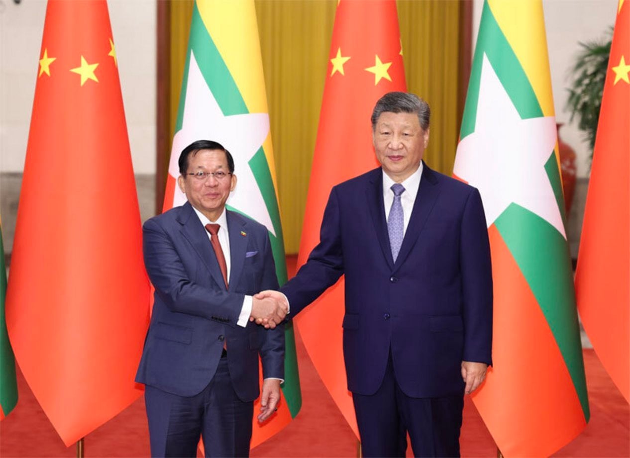 Two male leaders in dark suits shaking hands before Chinese and Myanmar flags at a formal bilateral diplomatic summit in Beij