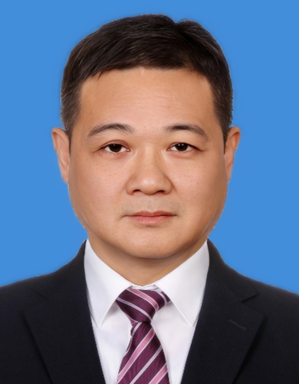 Middle-aged East Asian man in black suit, white dress shirt, and purple striped tie against a blue background, formal portrai