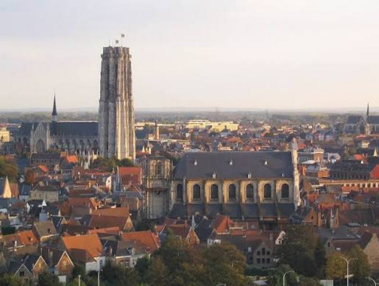 Aerial view of Mechelen Belgium featuring the unfinished Gothic tower of Saint Rumbold's Cathedral rising above terracotta ro