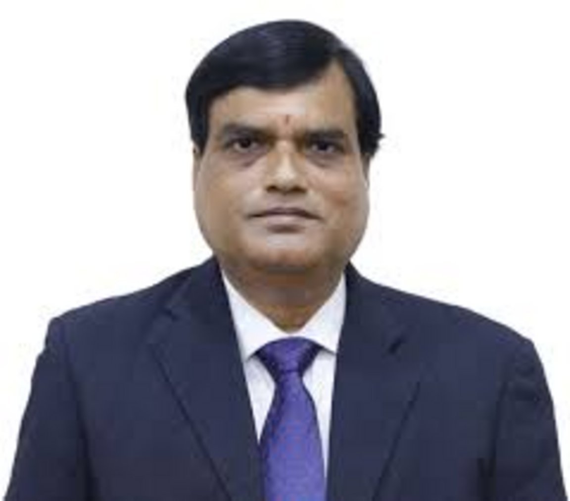 Middle-aged Indian man wearing a dark navy blazer, white dress shirt, purple tie, and a red tilak on his forehead, formal hea