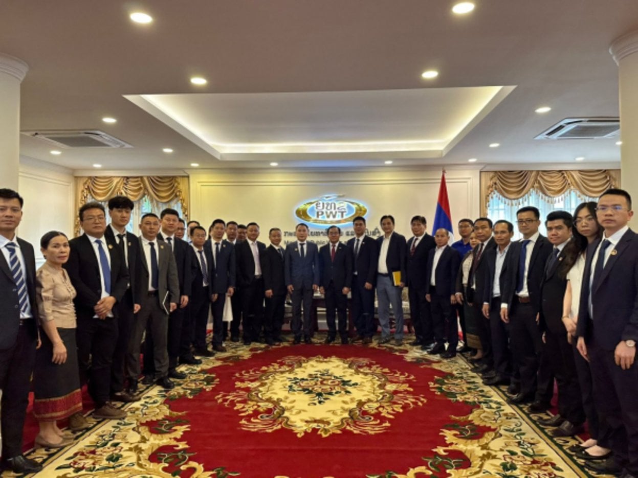 Large formal delegation of approximately 30 officials in business suits posing inside PWT Laos headquarters with red ornate c