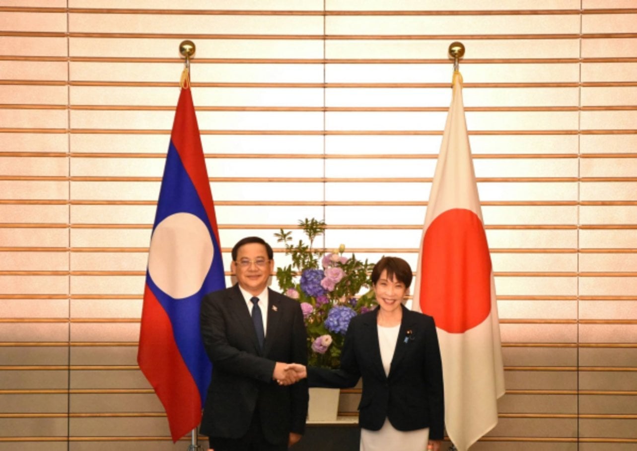 Two diplomats shake hands in formal meeting between the flag of Laos and the flag of Japan with floral arrangement