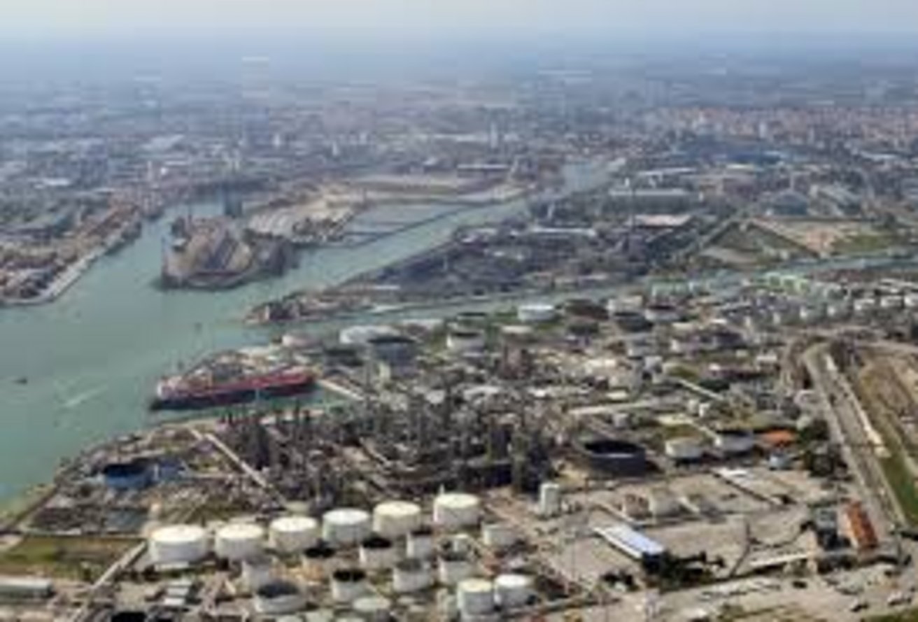 Aerial panorama of a large industrial petrochemical refinery complex along a busy shipping channel with oil storage tanks and