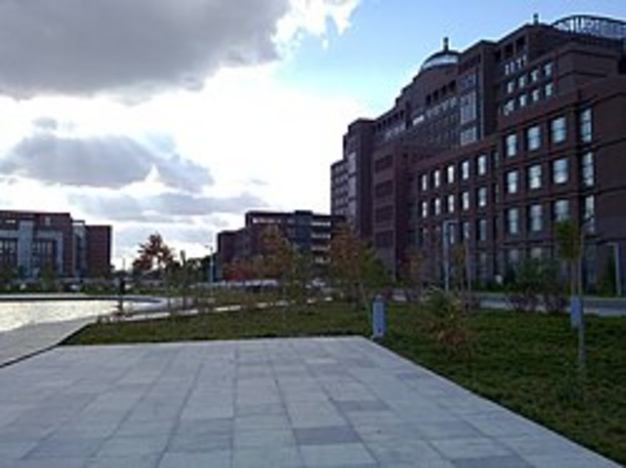 Multi-story red-brick urban residential and commercial buildings surrounding a green courtyard with stone pavers and young tr