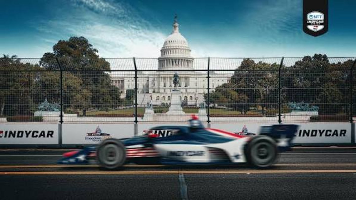NTT IndyCar Series open-wheel race car with American flag livery speeding past US Capitol Building on Washington DC street ci