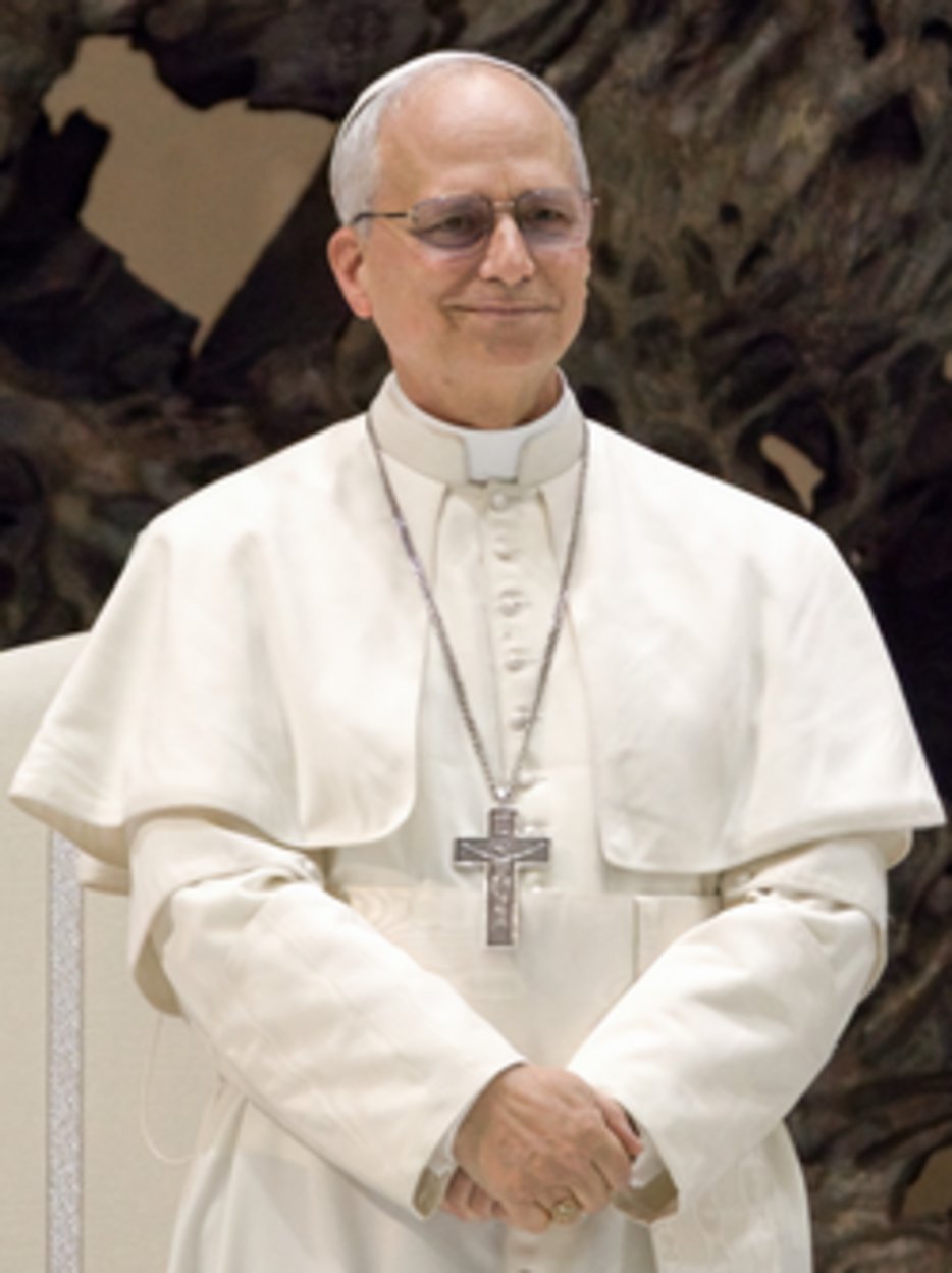 Senior Catholic bishop in white cassock and cape wearing pectoral cross on chain, zucchetto skullcap, and rimless glasses
