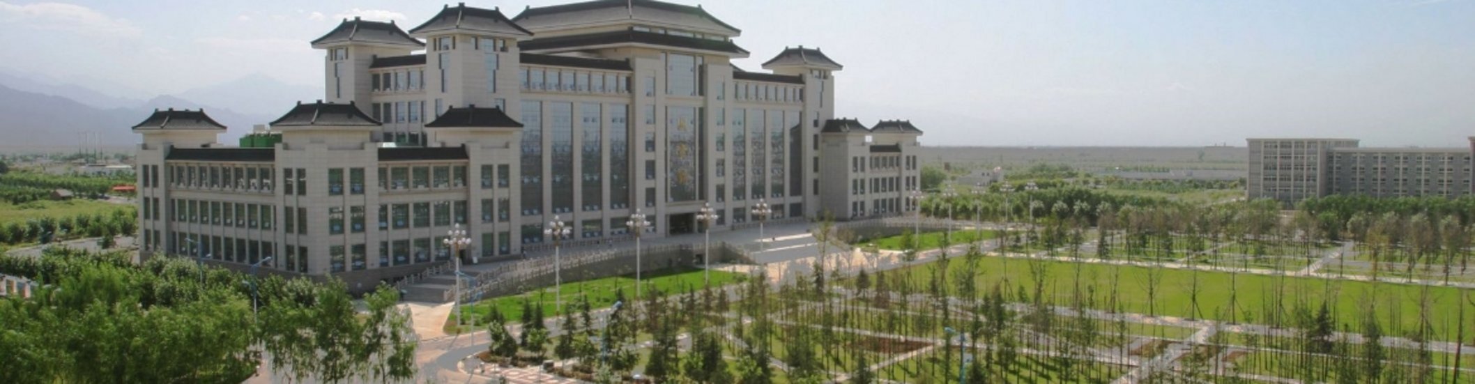 Large multi-story Chinese imperial-style administrative building with dark pagoda rooftops surrounded by green lawns and tree