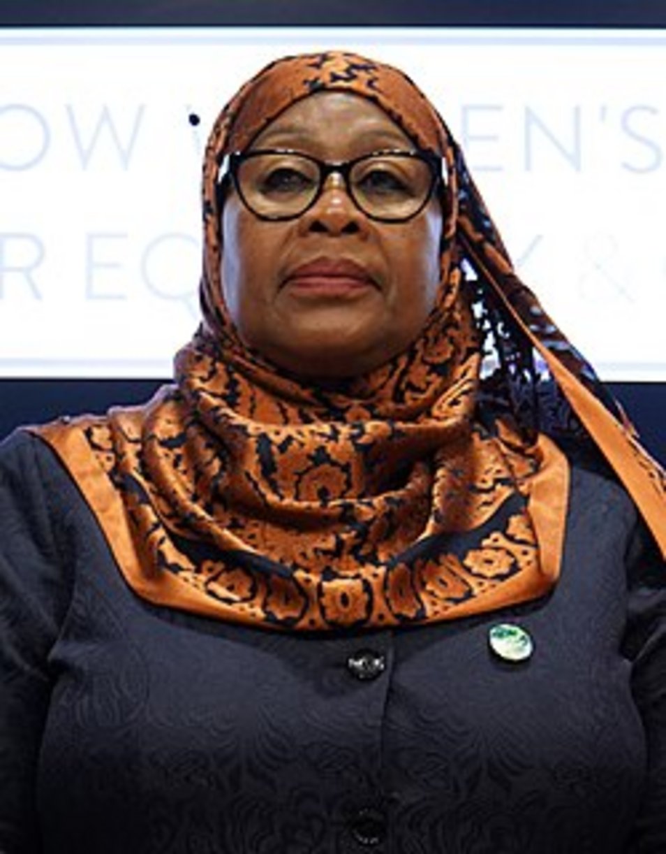 A woman in an ornate orange and black patterned hijab and dark blazer with glasses at a Women's Rights conference event