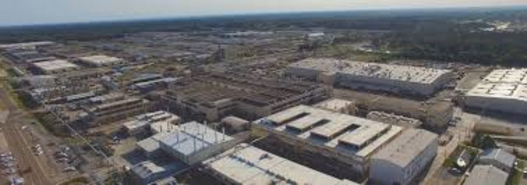 Panoramic aerial view of large industrial warehouse complex with multiple flat-roof buildings, active construction zone, and