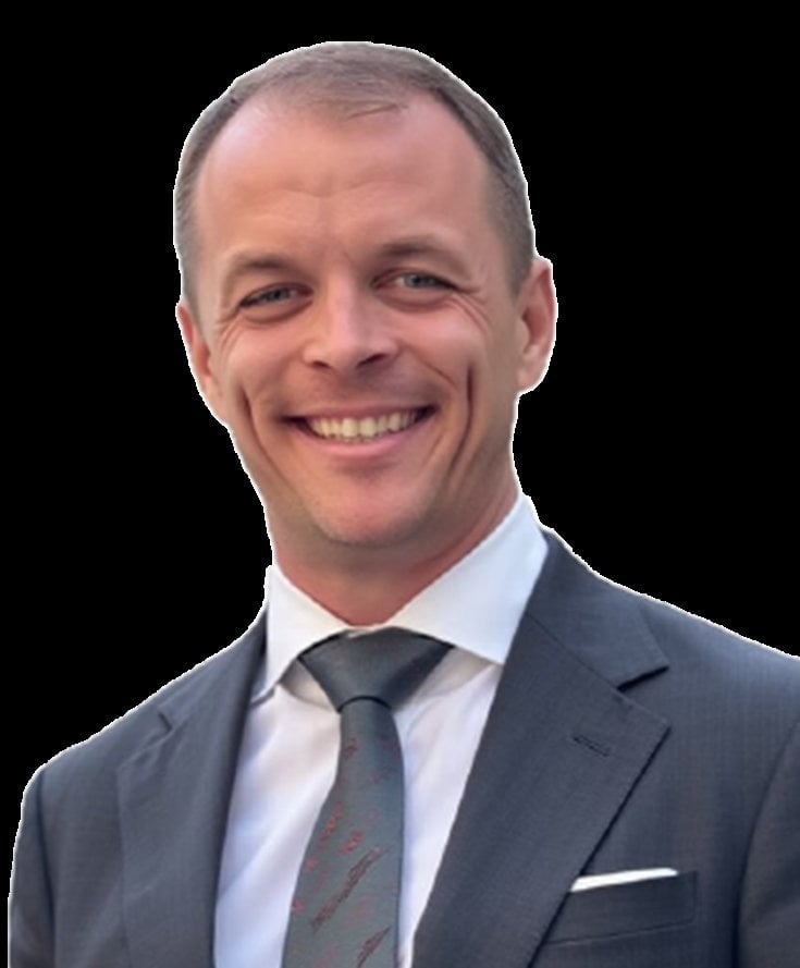 Smiling middle-aged man with short brown hair wearing a charcoal gray suit, white dress shirt, and patterned gray tie in a pr