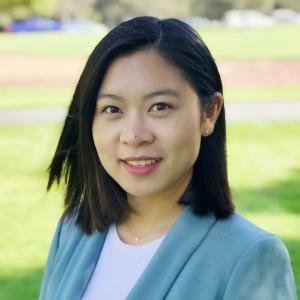 Young East Asian woman with shoulder-length black hair, wearing a teal blazer and white top, smiling warmly in an outdoor par