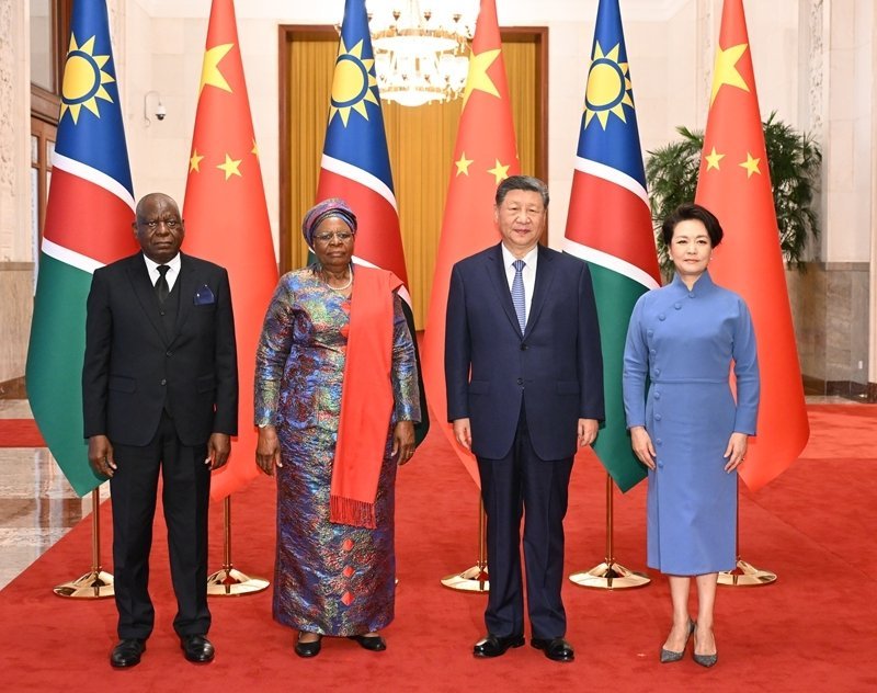 Four dignitaries standing before Namibian and Chinese flags on red carpet at formal state reception in Beijing