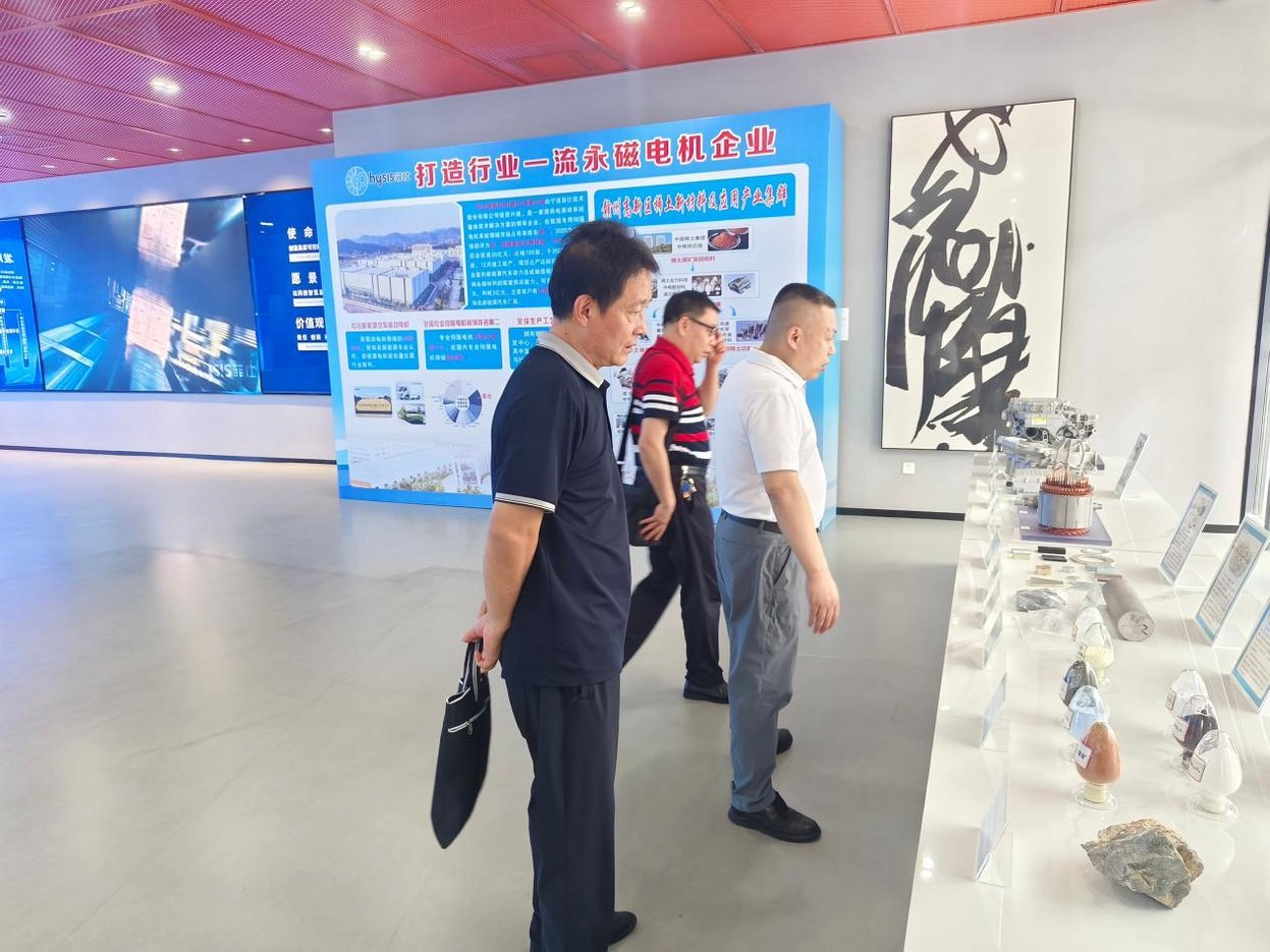 Three men touring Hyisis permanent magnet motor enterprise showroom with rare earth mineral samples and blue promotional disp