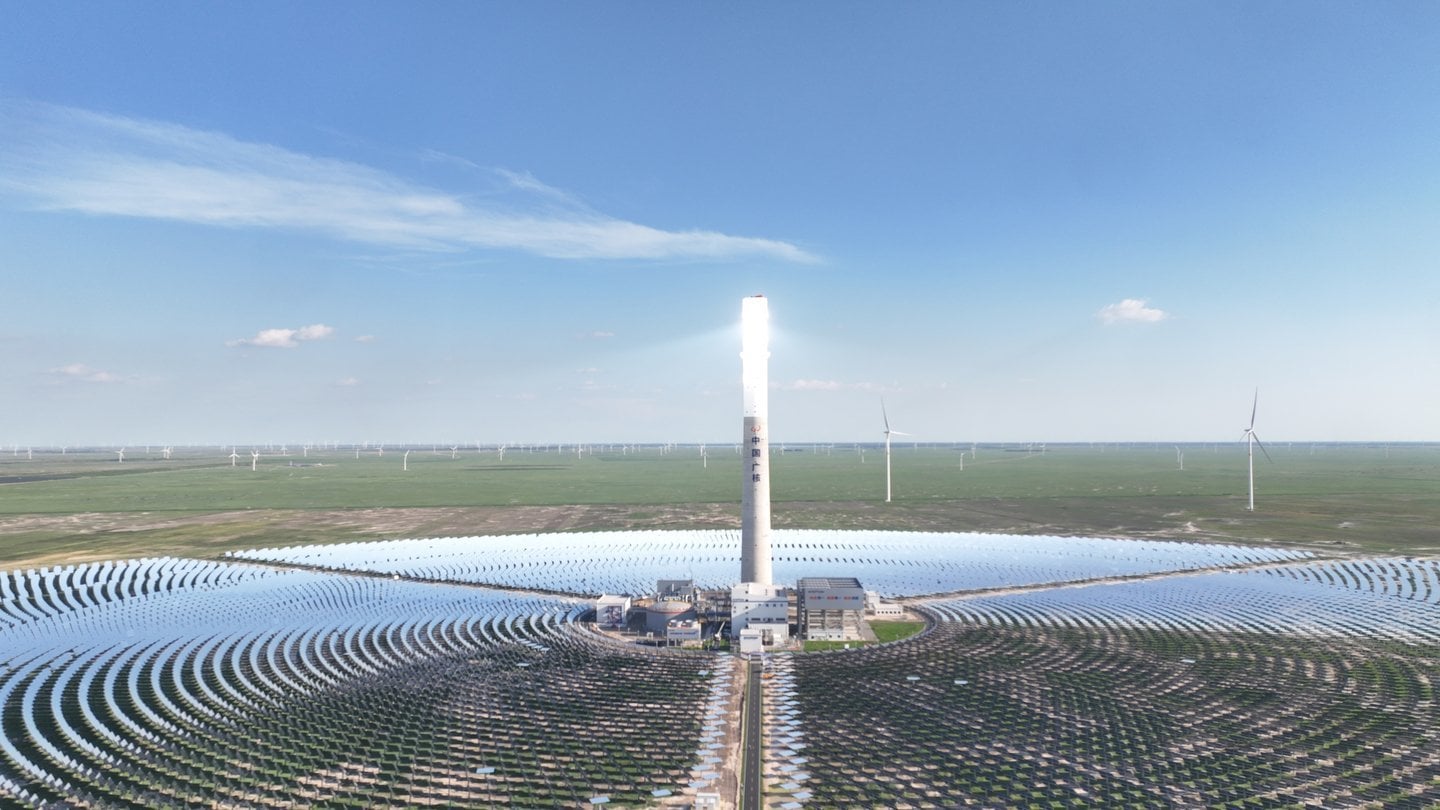 CGN concentrated solar power tower with glowing receiver surrounded by heliostat mirror field and wind turbines on flat plain