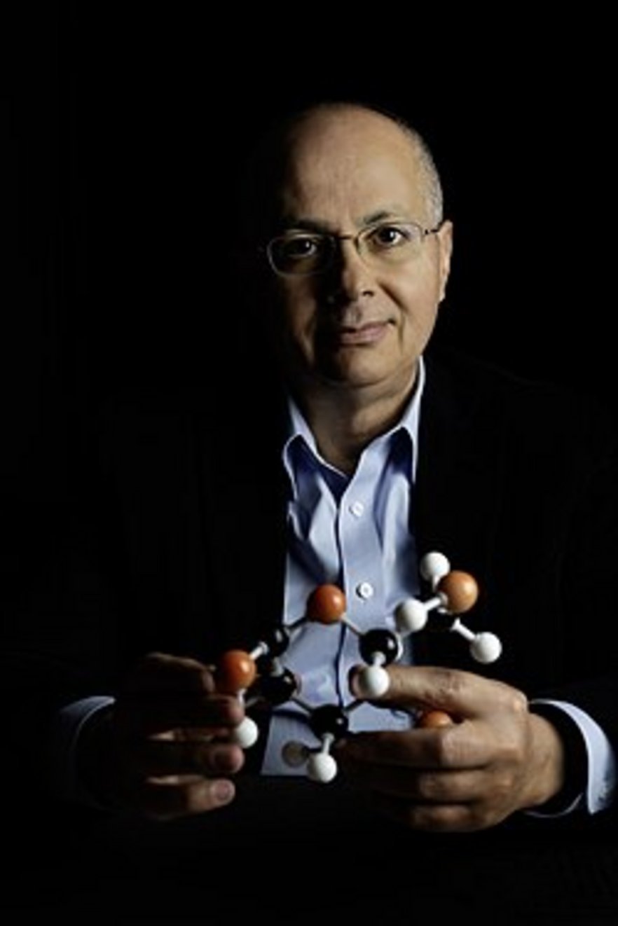 Middle-aged bespectacled man in blue shirt and dark blazer holding a colorful ball-and-stick molecular model against black ba