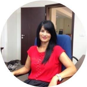 Smiling woman with long black hair wearing a red blouse, seated in a blue office chair at a workplace desk