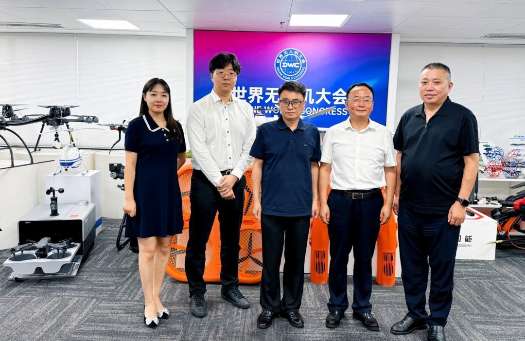 Five professionals pose at Drone World Congress DWC office in China, surrounded by UAV models and drone equipment displays