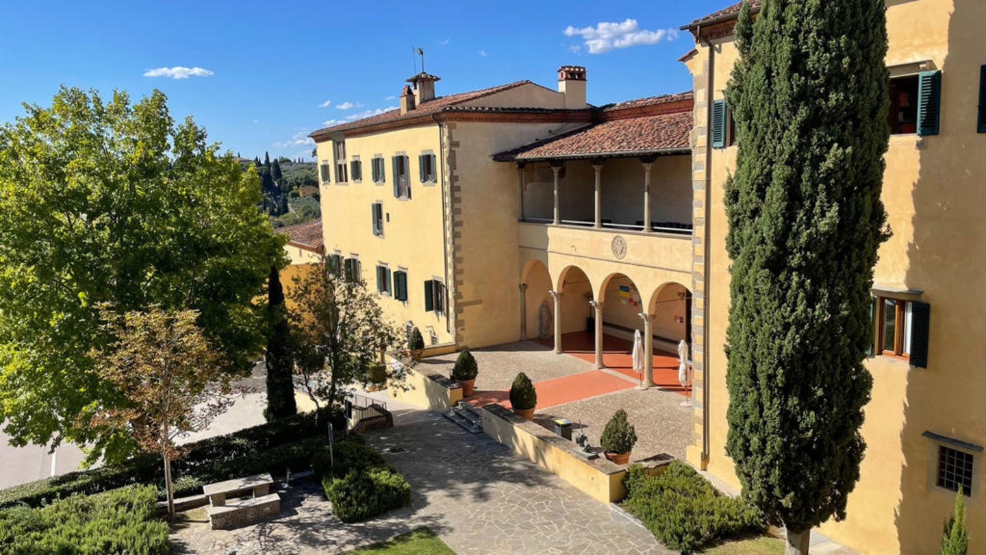 Yellow ochre Renaissance villa with arched loggia, cypress trees, and terracotta courtyard in Fiesole, Tuscany, Italy