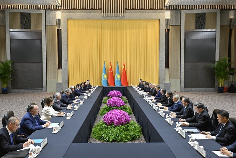 Kazakhstan and Chinese delegations seated at formal bilateral meeting table with Kazakhstan and Chinese flags displayed at ce