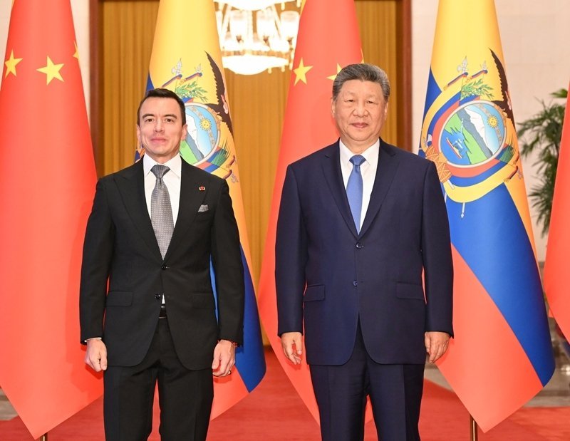 Two men in dark suits standing before Chinese and Ecuadorian flags during a formal bilateral diplomatic meeting