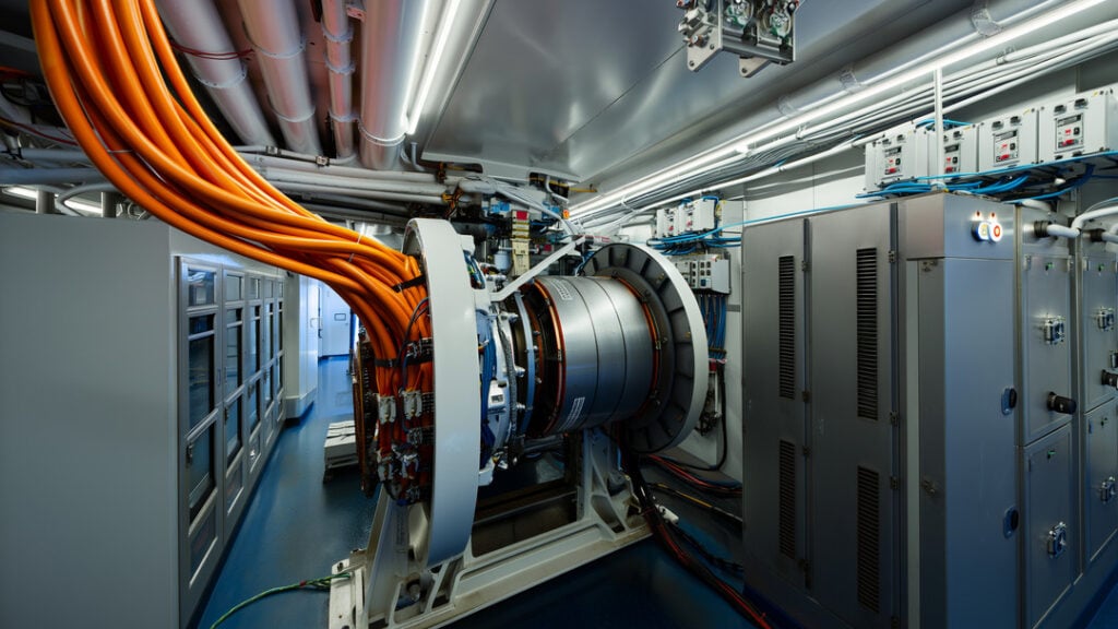 Photorealistic wide-angle view inside a modern ferry machinery room showcasing electric ship propulsion with a permanent-magnet motor, azimuth pod coupling, orange high-voltage cables, VFD cabinets, switchboard, and lithium-ion battery racks amid stainless piping and cable trays.