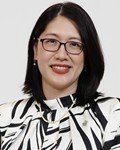 Smiling Asian woman with glasses and short black hair wearing a black and white patterned blazer in a professional headshot