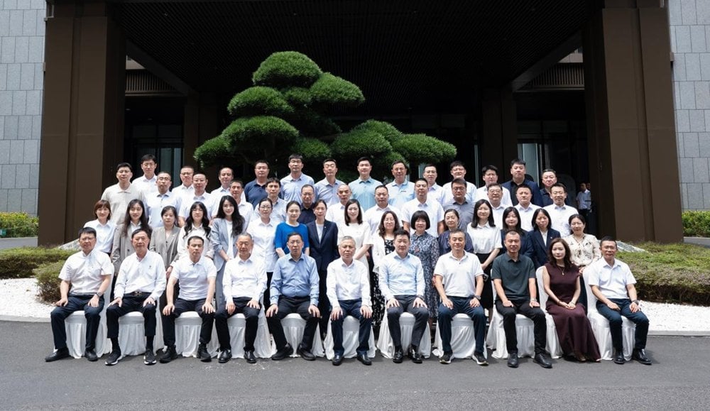 Large group of approximately 50 business professionals posed in formal rows outside modern corporate headquarters with sculpt