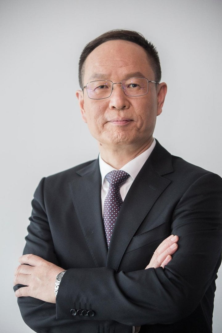 Middle-aged Asian man in black suit and patterned burgundy tie with glasses, arms crossed, silver watch, formal corporate hea