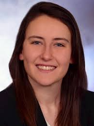 Young woman with shoulder-length dark brown hair smiling in a professional headshot wearing a dark blue blazer