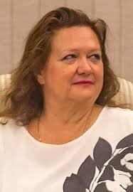 A middle-aged woman with shoulder-length brown hair wearing a white and gray floral blouse seated in a formal indoor setting