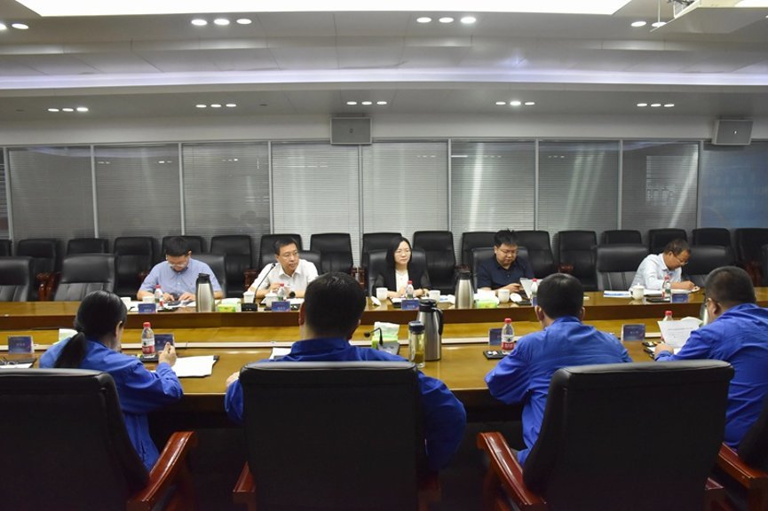 Five executives seated facing blue-uniformed workers across large wooden conference table in Chinese corporate boardroom with