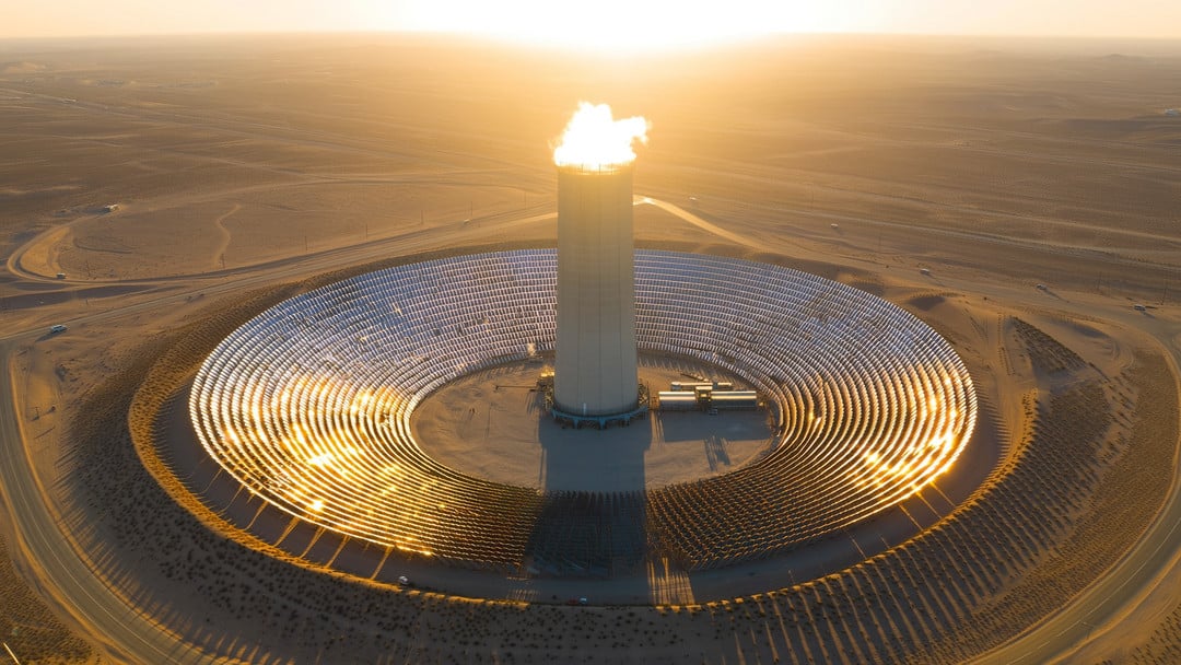 Solar thermal towers Photorealistic wide-angle aerial view of **solar thermal towers** in a sunlit desert, showing thousands of heliostat mirrors focusing sunlight onto a tall central receiver tower with a glowing top, molten-salt storage tanks and a turbine hall below, heat shimmer, dusty access roads, and long late-afternoon shadows.