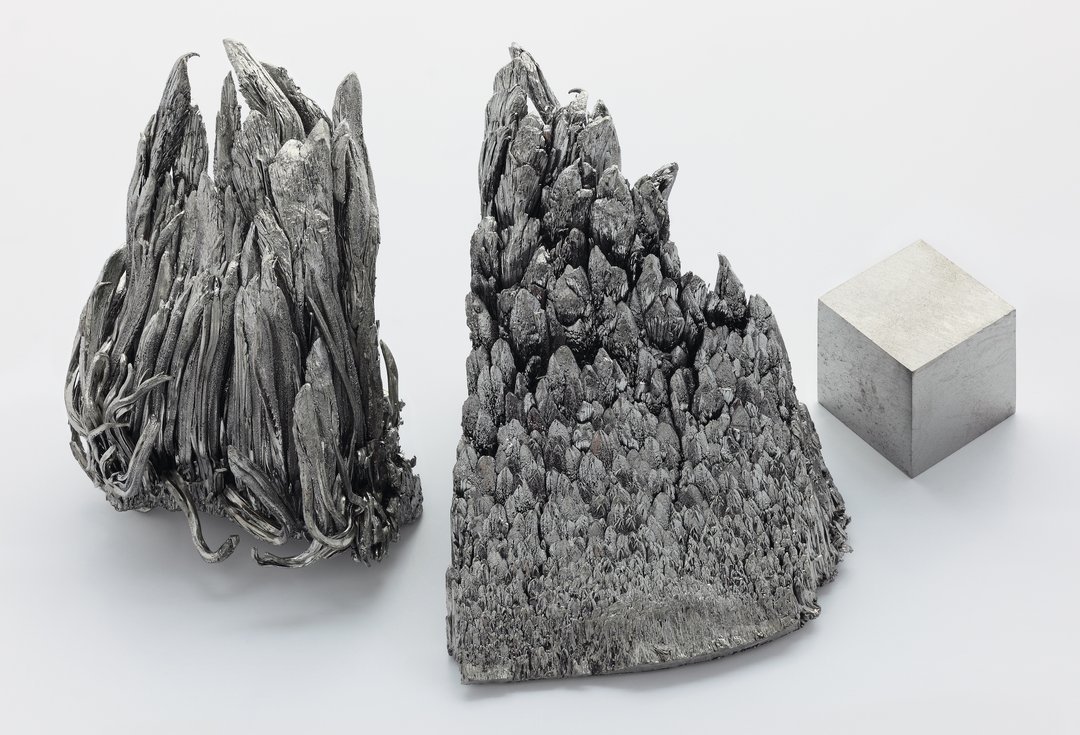 Three specimens of pure scandium metal: two crystalline dendritic formations with jagged spiky textures and one machined poli